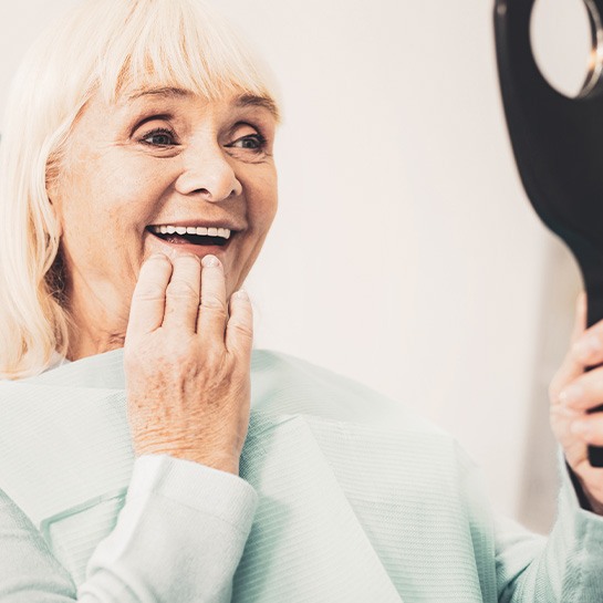 An older woman admiring her new dentures in a hand mirror