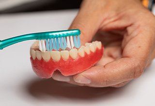 An older patient brushing their denture