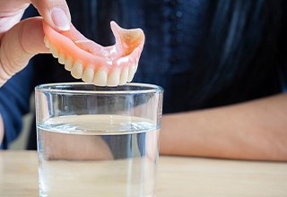 Someone placing dentures in a glass of water