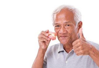 Man holding his dentures with a thumbs up