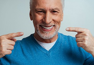 Man in blue shirt pointing to his dentures with two fingers smiling