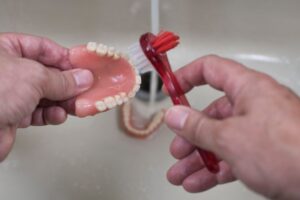 Person brushing their dentures over a sink