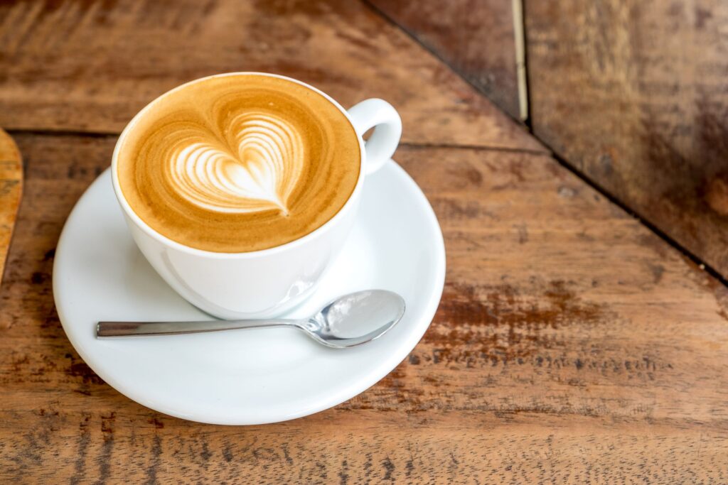 Cup of coffee with foam heart on a white saucer on a wooden table